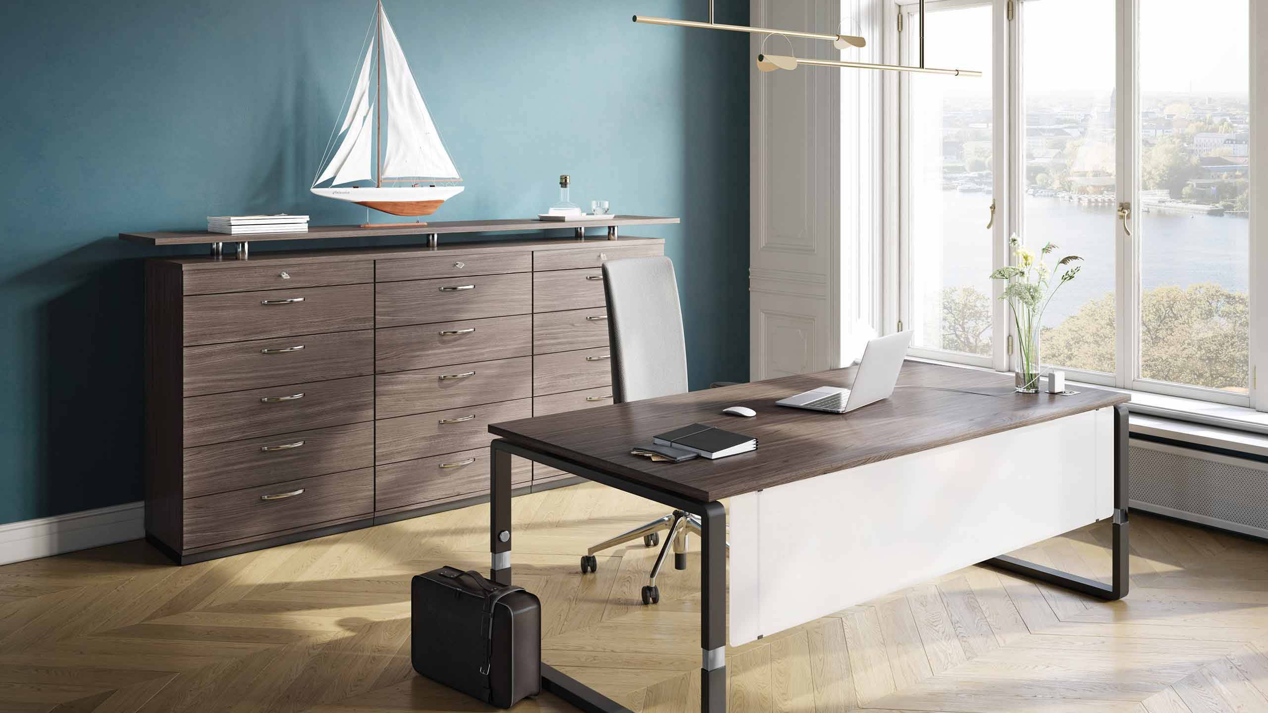 Home-Office mit Schreibtisch, Sideboard und Pendelleuchte vor blauer Wand